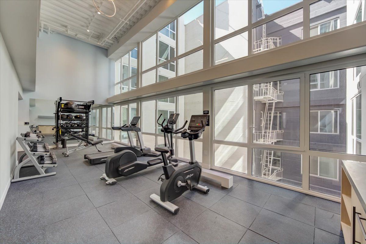 Gym with exercise equipment, including treadmills and weights, next to large windows.