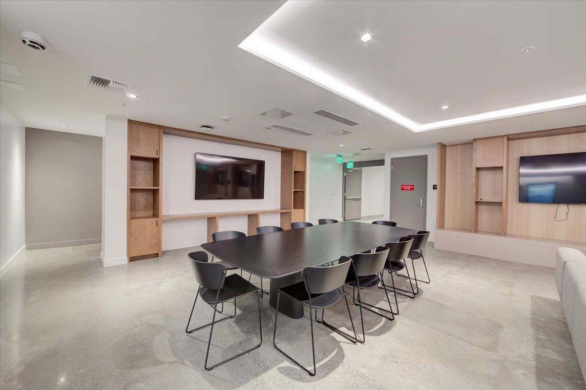 Conference room with large table, chairs, screens, wood cabinets, and polished concrete floor.