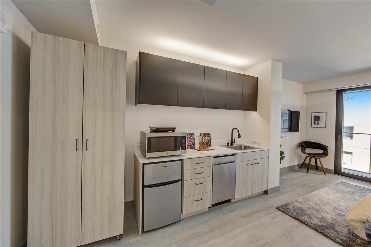 Small apartment kitchen with mini fridge, microwave, sink, cabinets, and a tall cabinet.