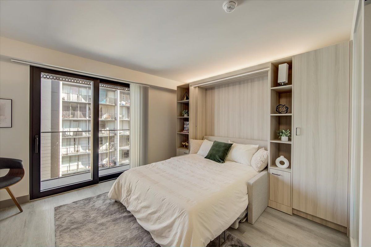 Bedroom with a bed, shelving, a sliding glass door to a balcony, and a fluffy rug on the floor.