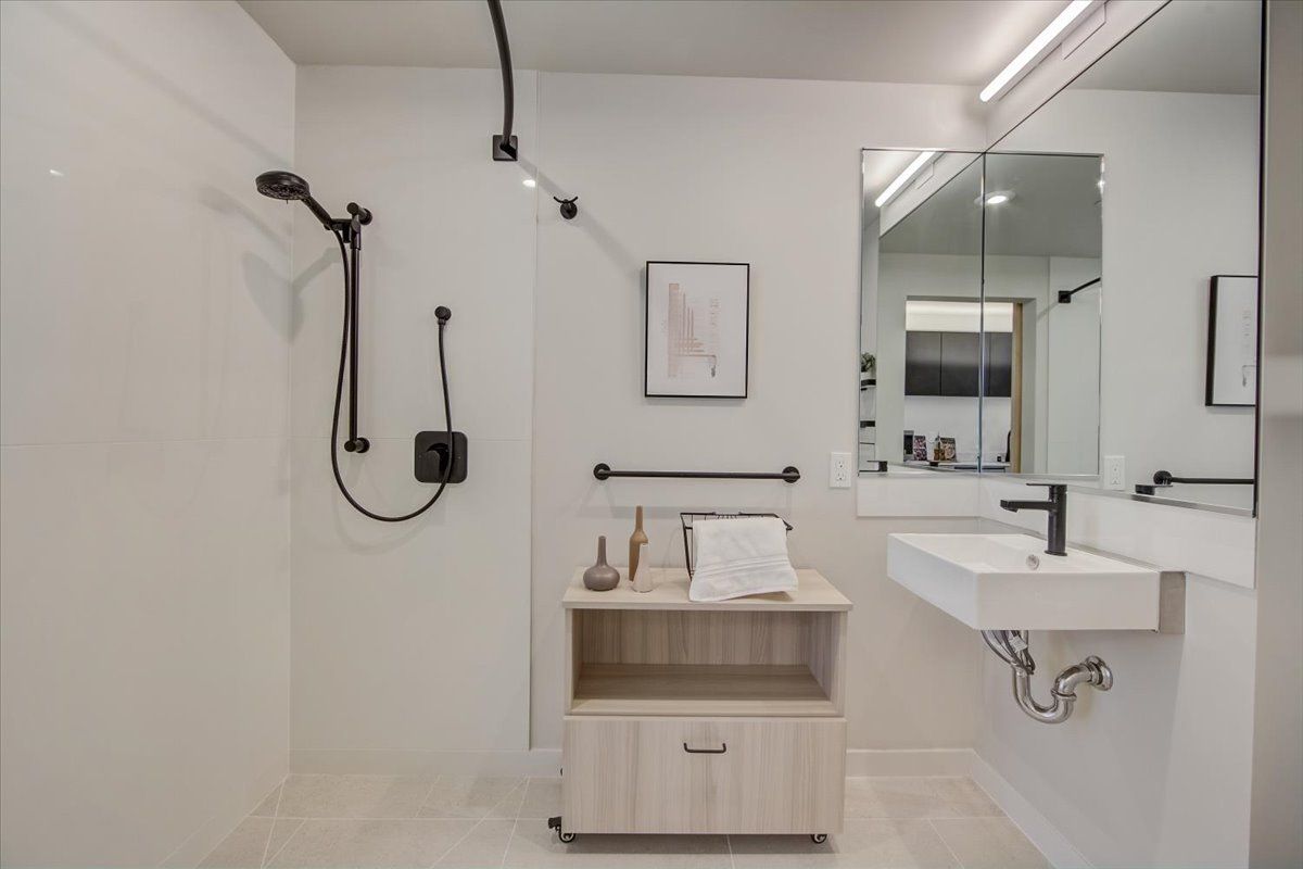 Bathroom with white walls, black shower fixtures, floating sink, light wood cabinet.