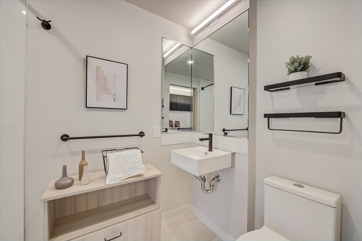 Modern bathroom with white walls, floating sink, and black fixtures. Includes a toilet and storage shelf.