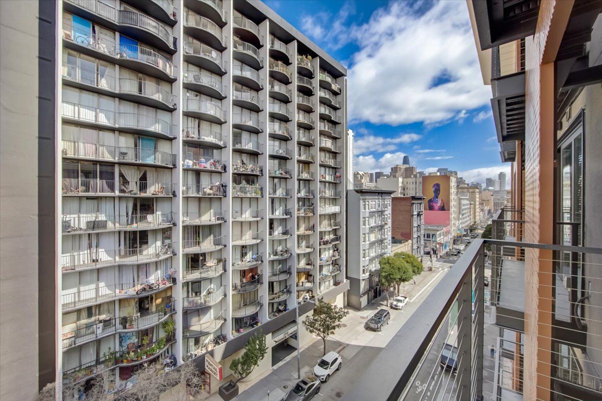View from a balcony overlooking a city street with tall buildings and a blue sky with clouds.