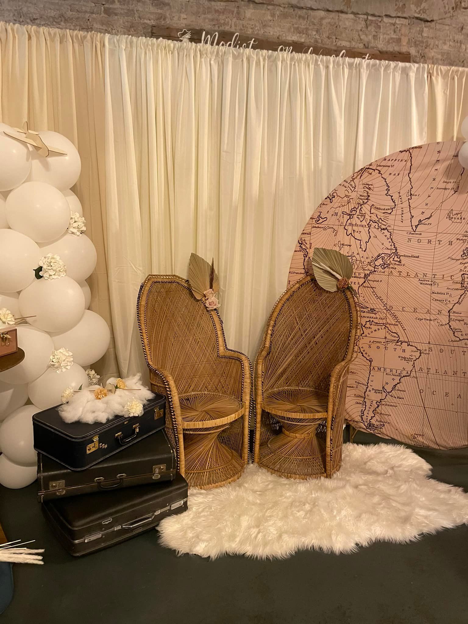 A room with wicker chairs , suitcases , balloons and a rug.