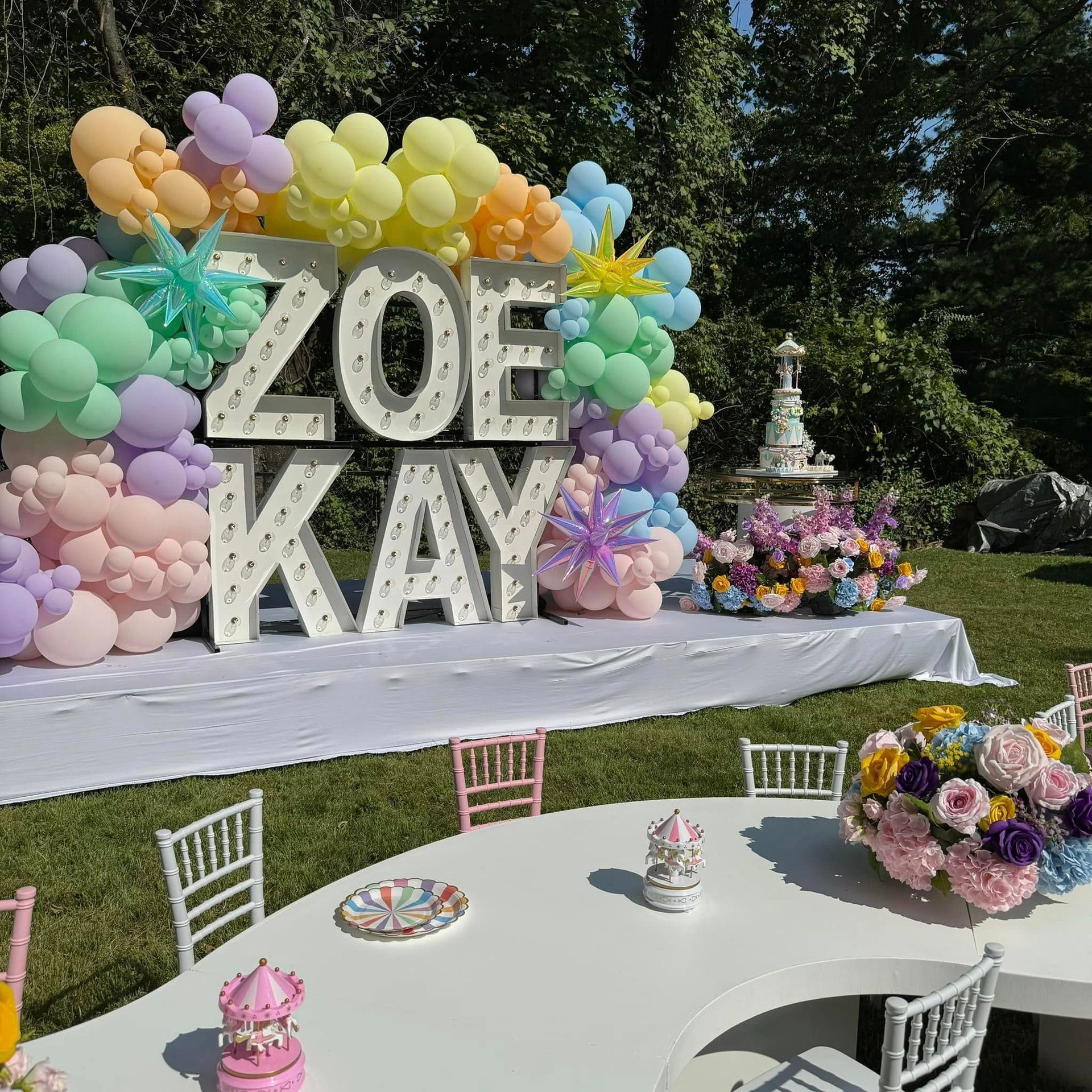 A table with a cake and balloons in front of a sign that says zoe kay