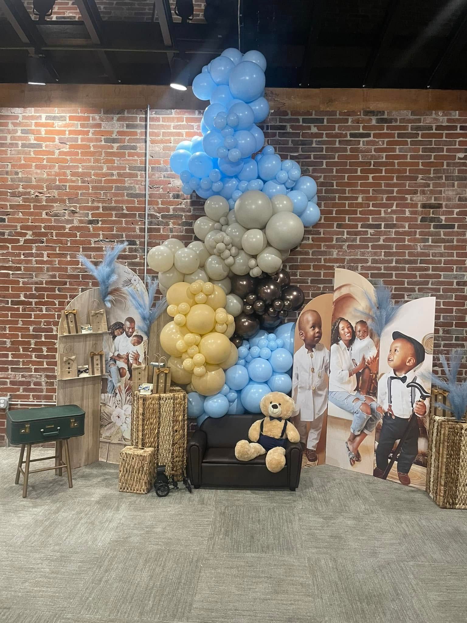 A room with balloons and a teddy bear in front of a brick wall.
