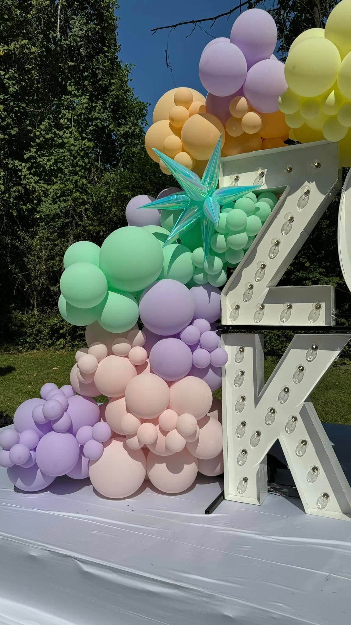 A large letter k is surrounded by balloons on a table.