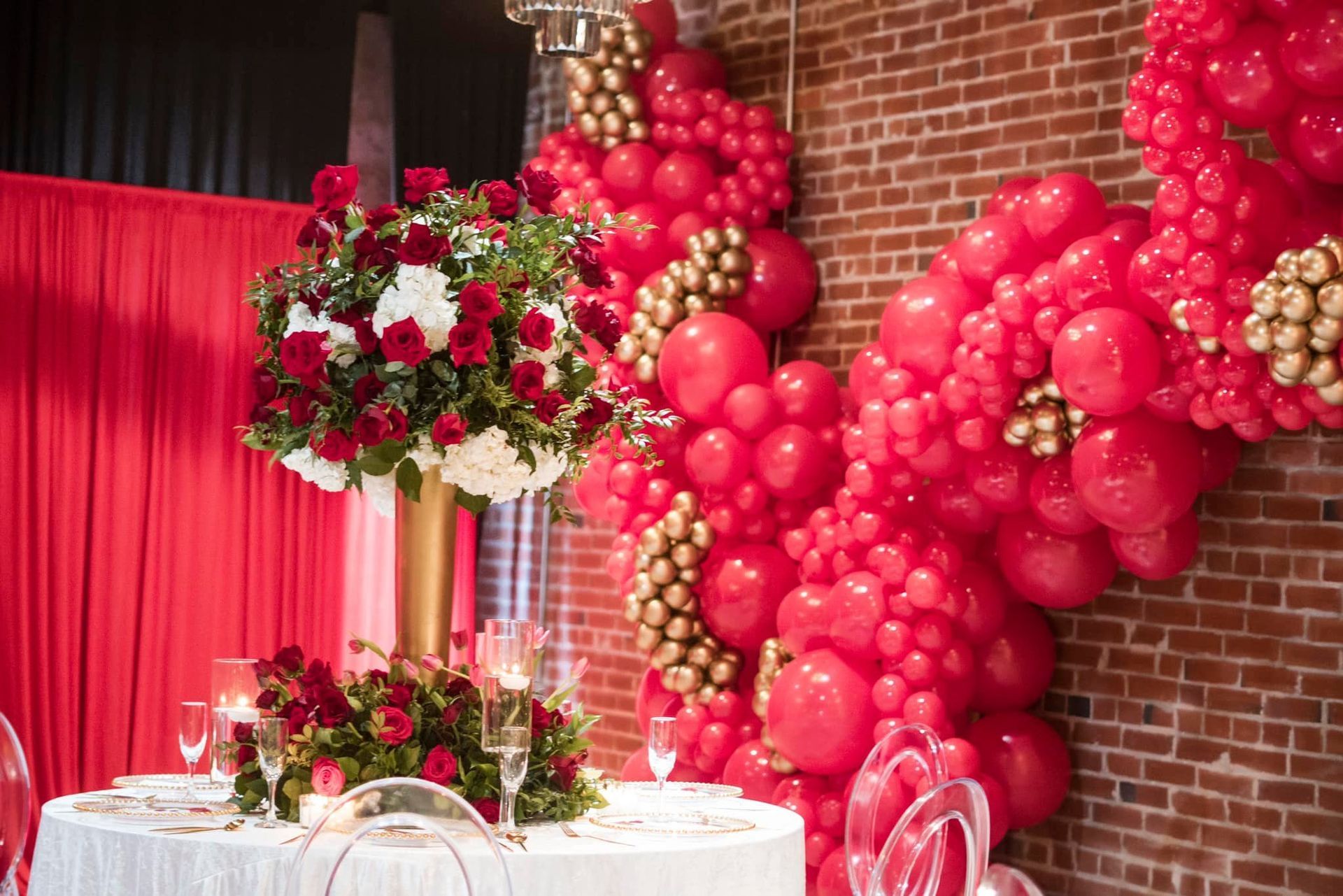 A table with flowers and balloons on it in front of a brick wall.
