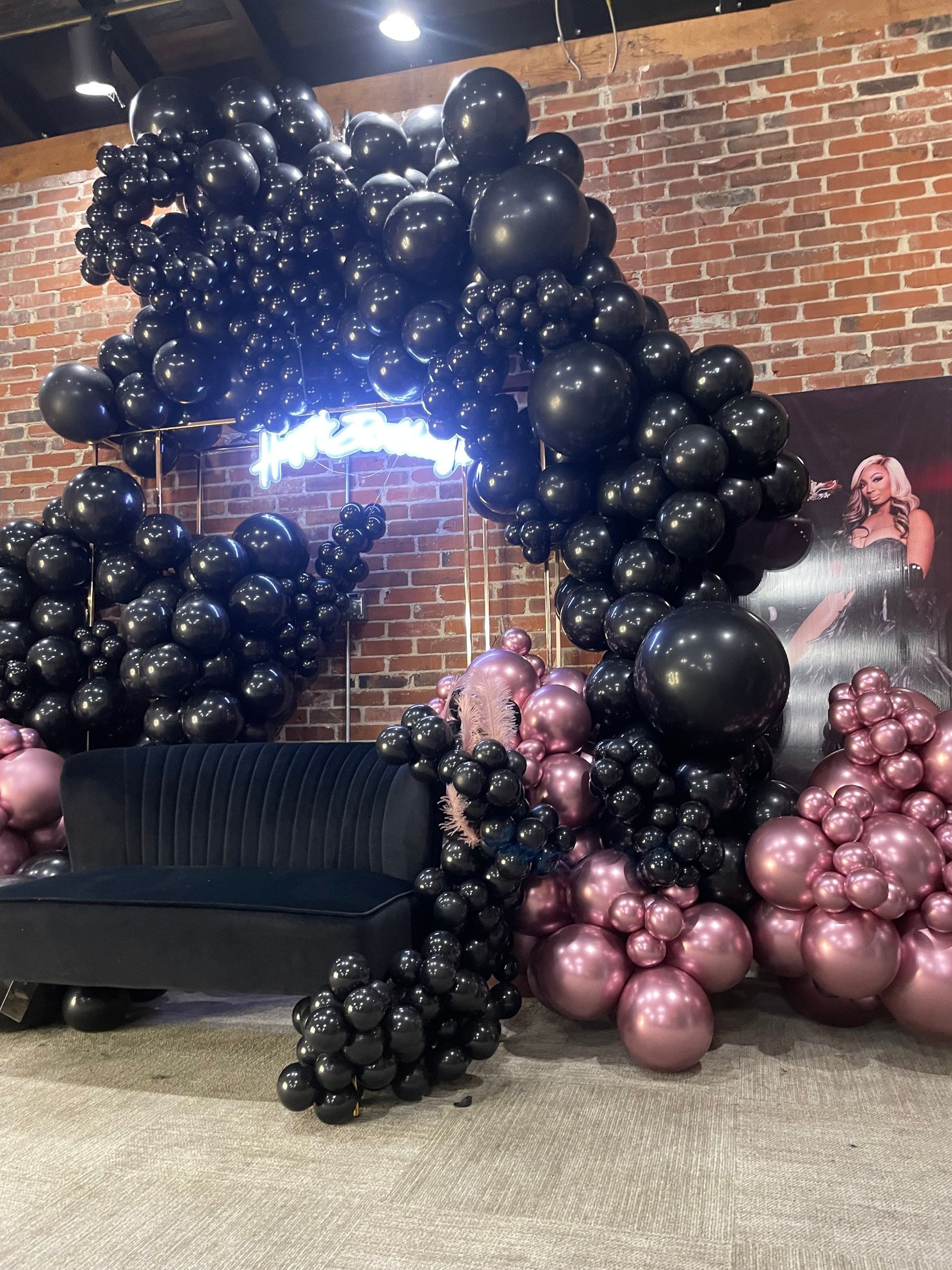 A bunch of black and pink balloons are sitting in front of a brick wall.