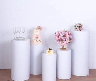 A group of white cylinders with a cake and flowers on them.