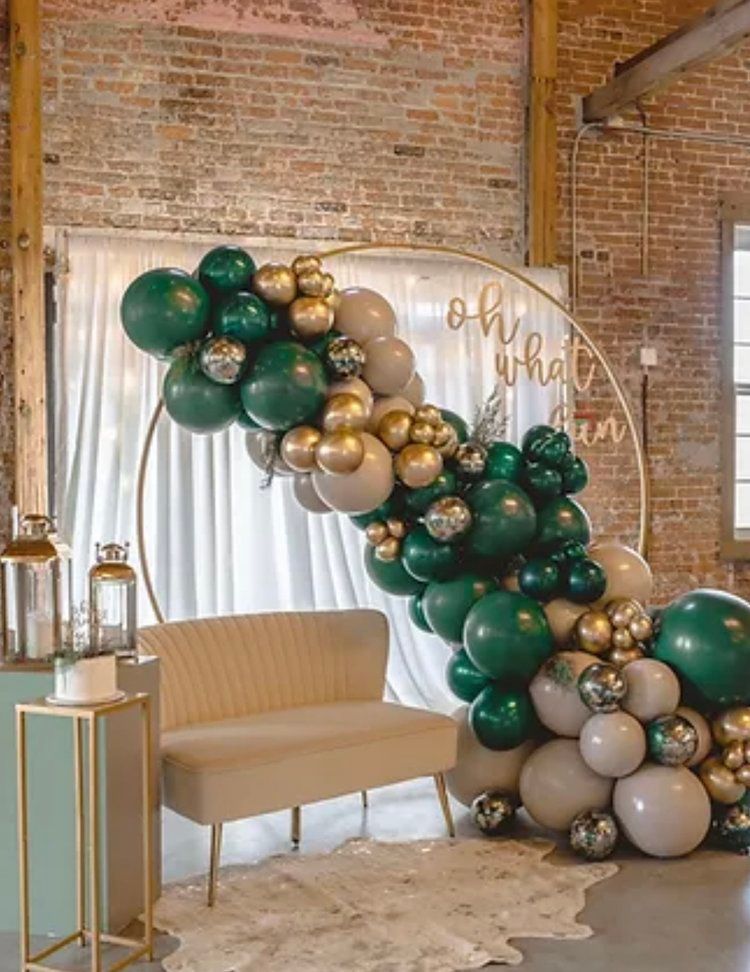 A couch is surrounded by green and gold balloons in a room.