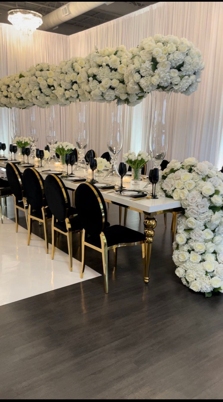 A long table with black chairs and white flowers hanging from the ceiling.