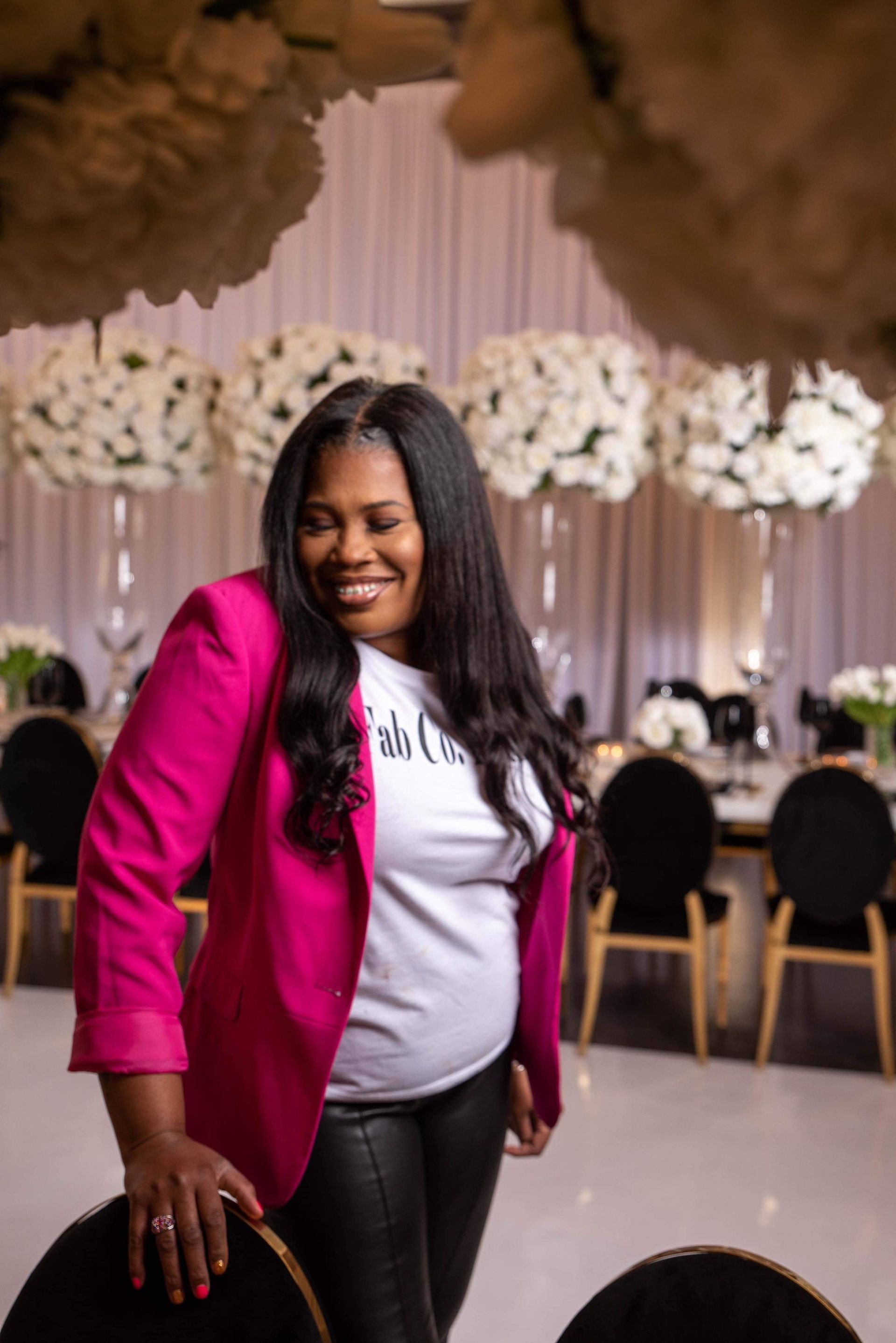 A woman in a pink jacket is standing next to a chair in a room.