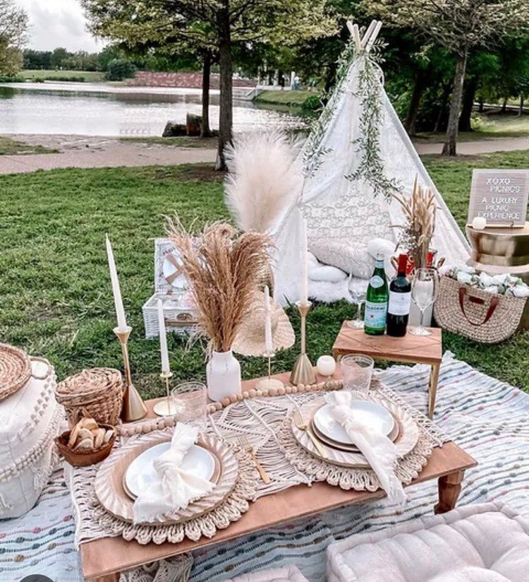 A picnic table with plates , wine bottles , candles and a teepee in the background.