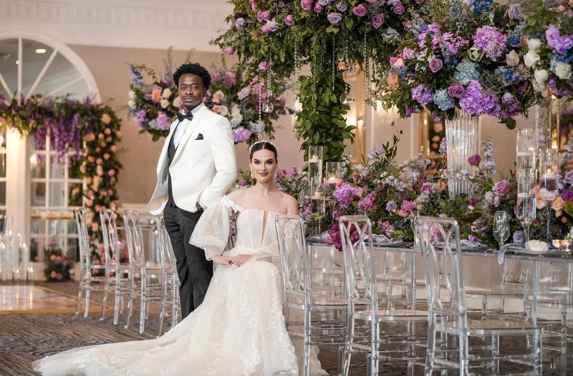 A bride and groom are posing for a picture in front of a table with flowers.