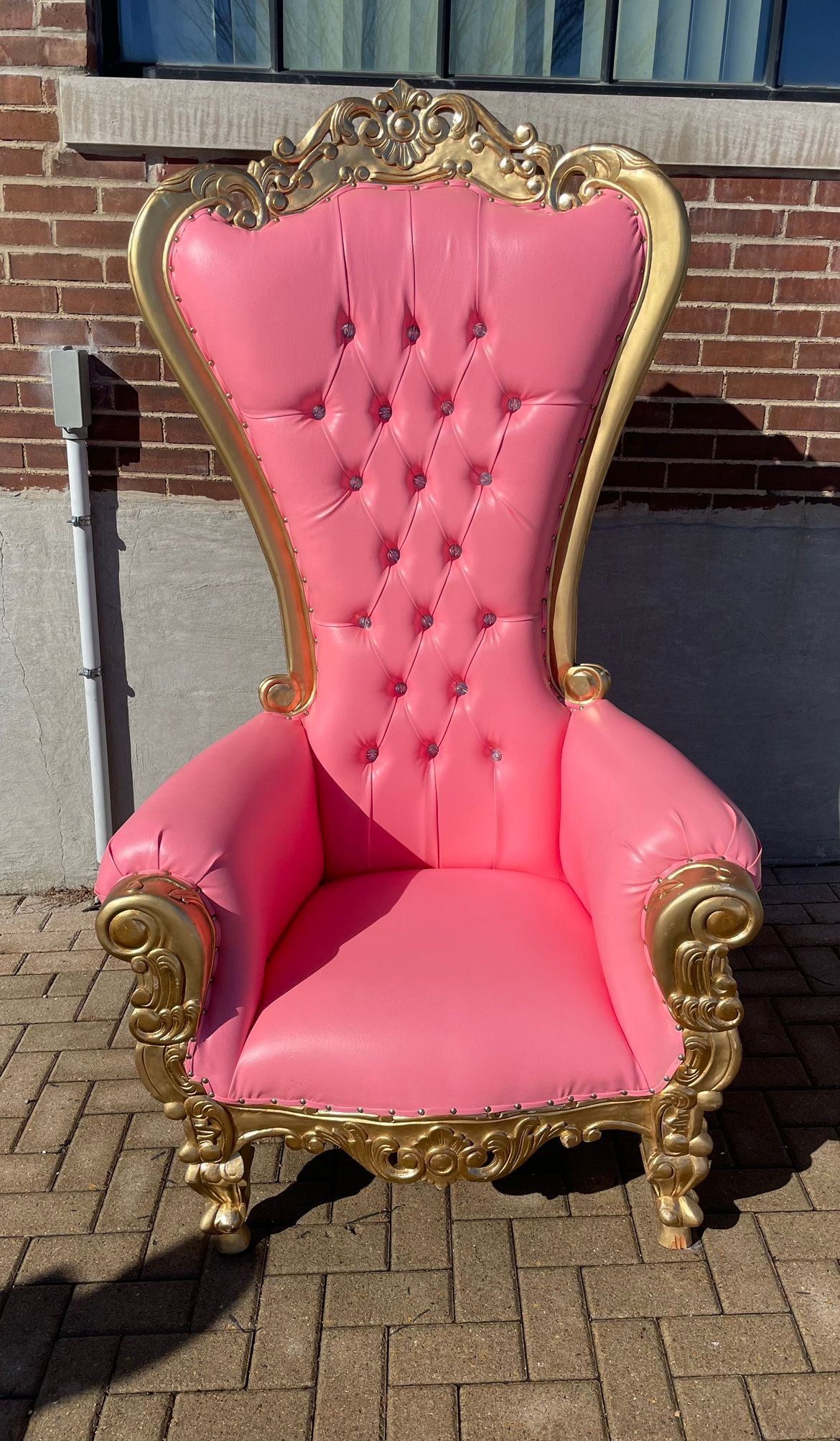 A pink and gold chair is sitting on a brick sidewalk in front of a brick building.