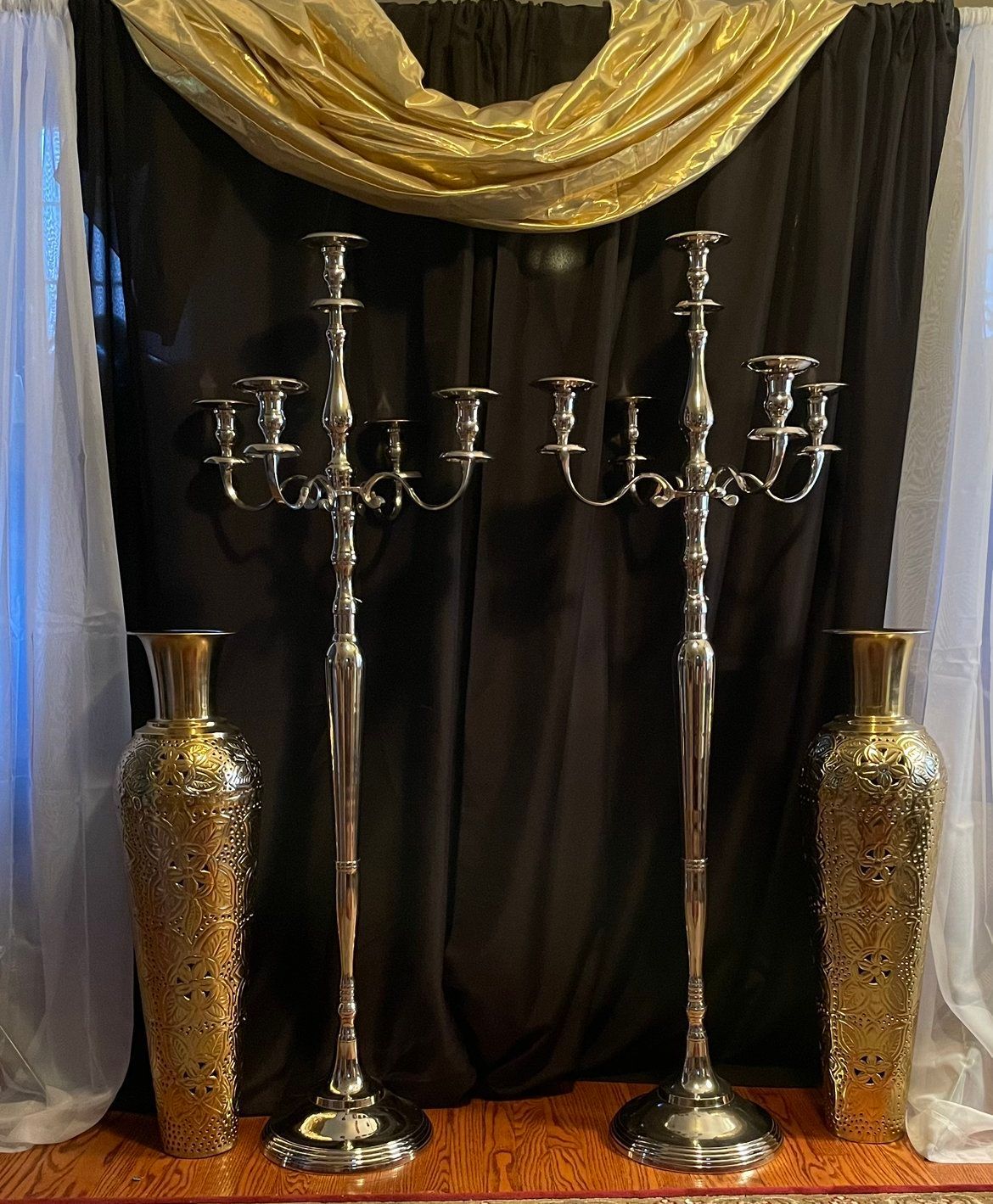 A row of silver candelabra and vases in front of a black curtain