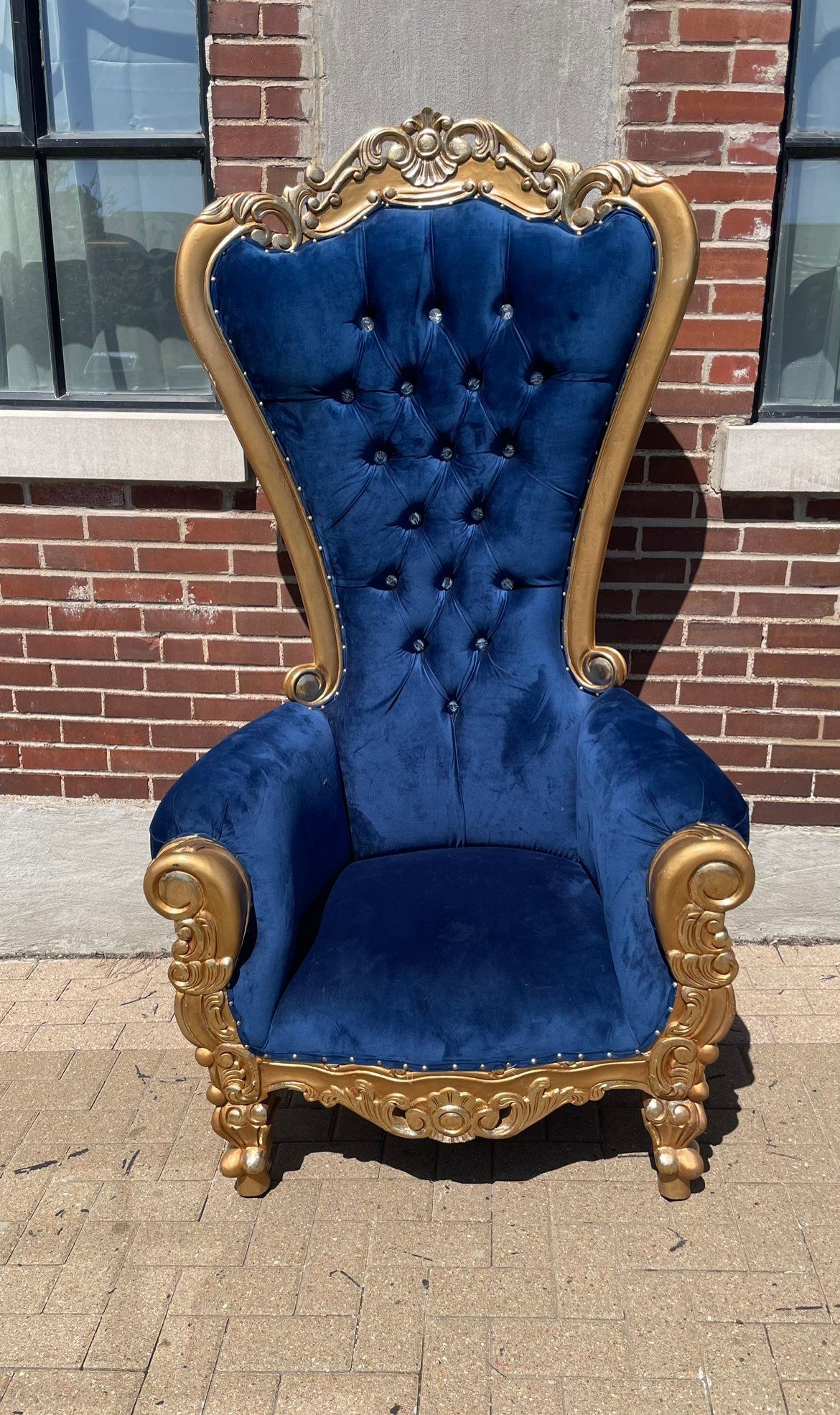 A blue and gold chair is sitting in front of a brick building.