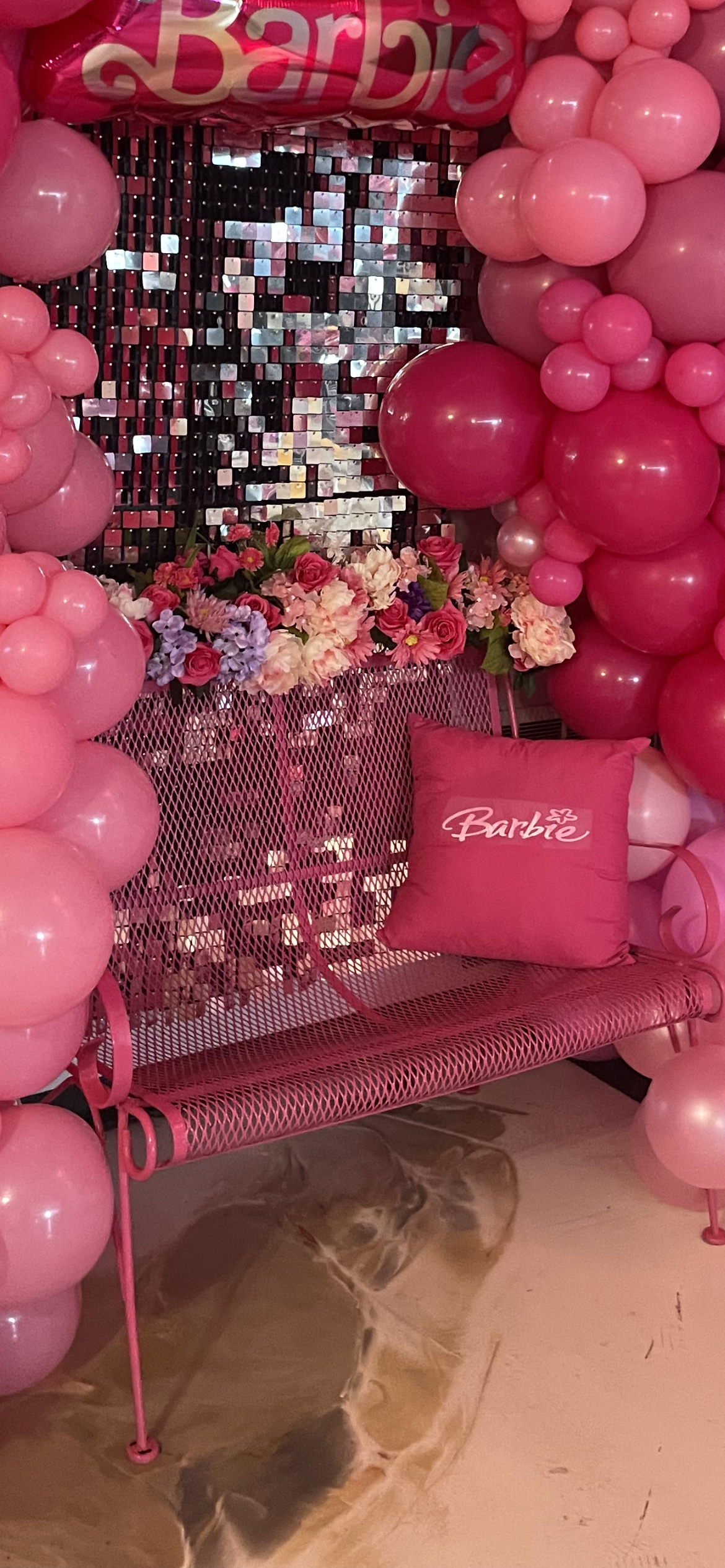 A pink bench is surrounded by pink balloons and flowers.