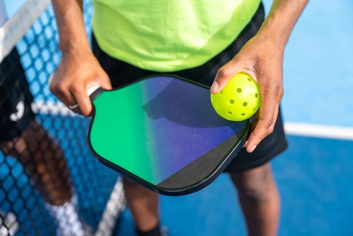 A person is holding a paddle and a tennis ball on a tennis court.