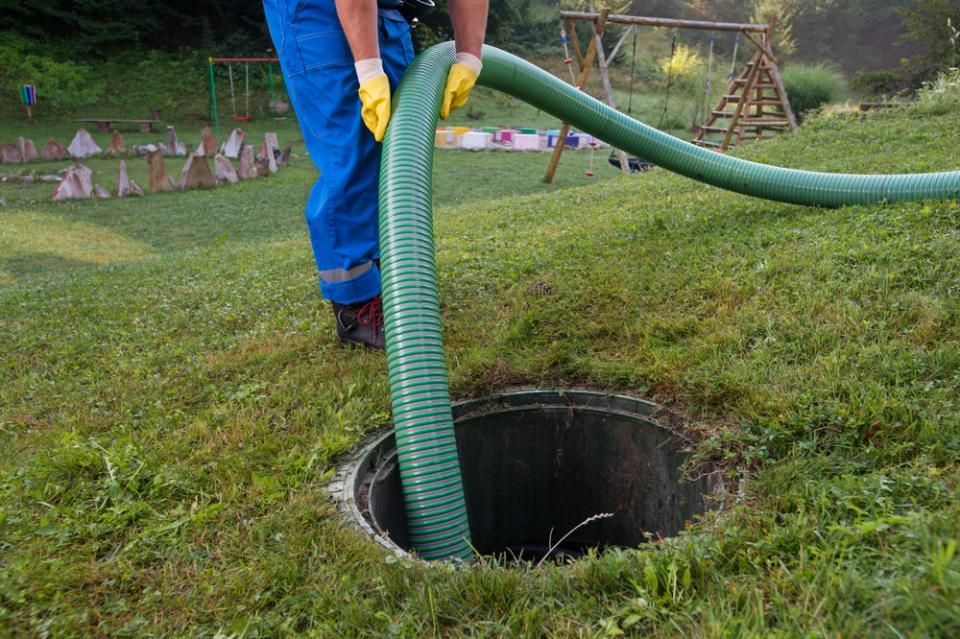 A Man Is Pumping Sewage Into A Septic Tank With A Green Hose — Paap's Cleansing Services In Burrum Heads, QLD