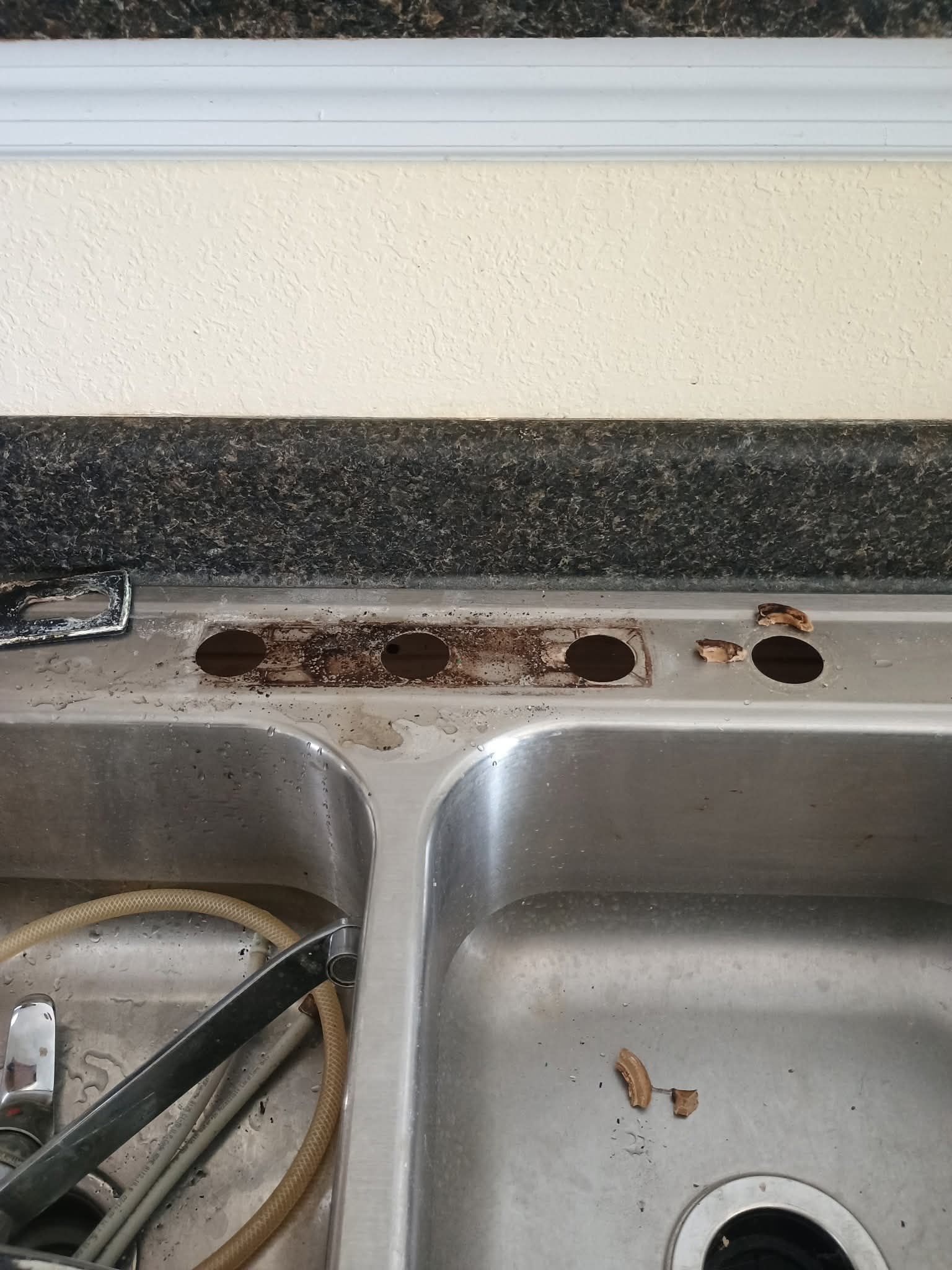 A dirty kitchen sink with holes in the counter top