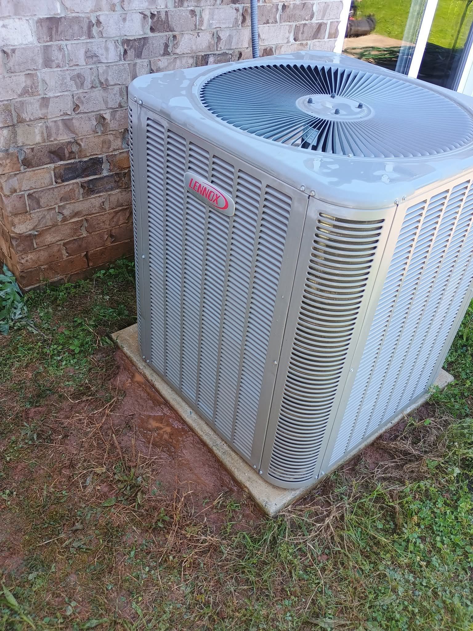 A large air conditioner is sitting in the grass in front of a brick building.