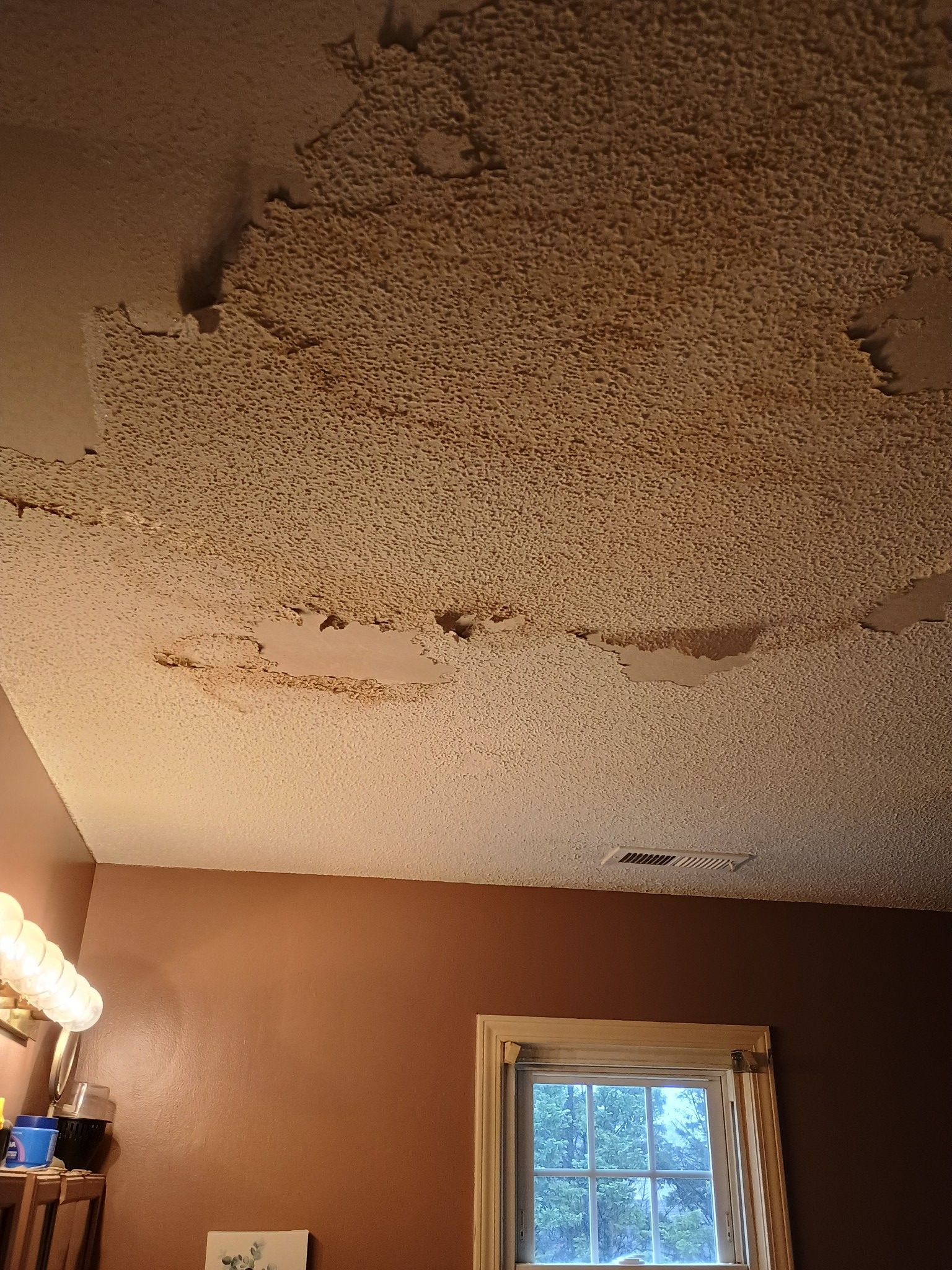 A room with a ceiling that is peeling and a window.