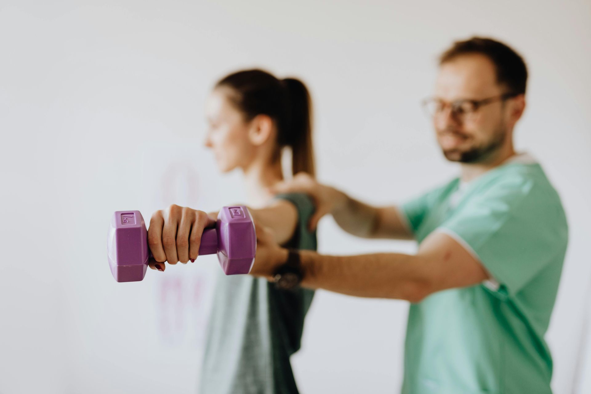 A chiropractor massaging a woman who is holding a dumbbell