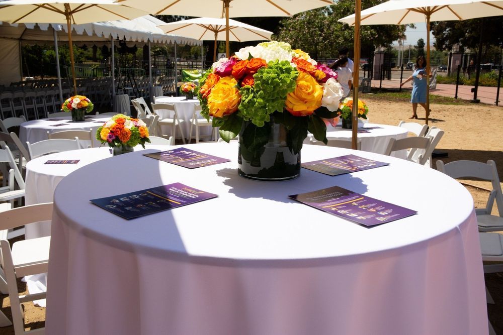 Outdoor event tables set with white tablecloths, flowers, and menus.
