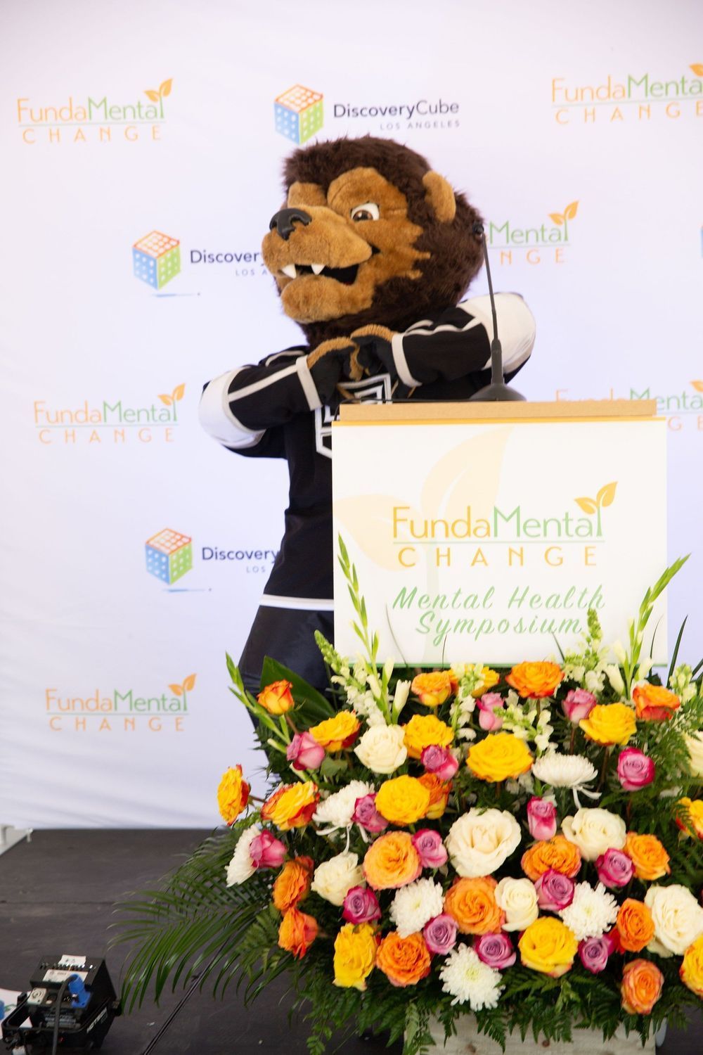 Lion mascot at mental health symposium podium with flowers.