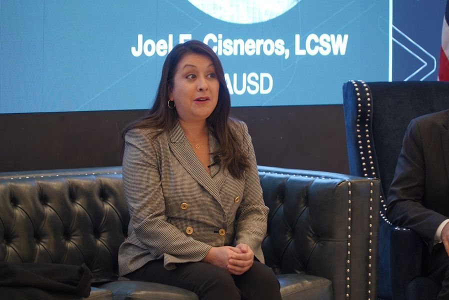 Woman in a blazer speaking on a panel, text behind her reads