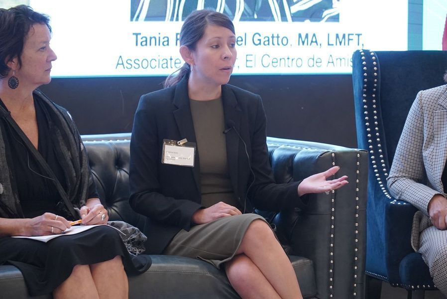 Panel discussion with three women seated on a black leather couch. Tania F. Del Gatto speaks, gesturing with her hand.