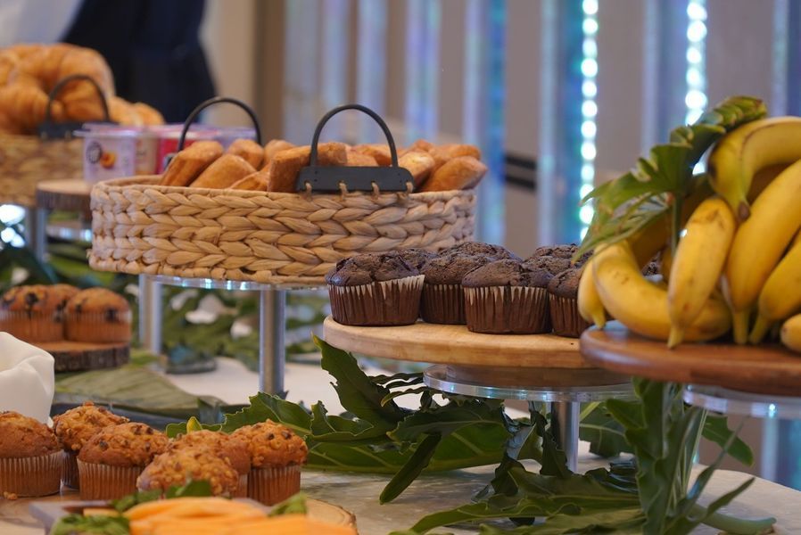 A buffet table featuring assorted muffins, bananas, and bread displayed on tiered platters.