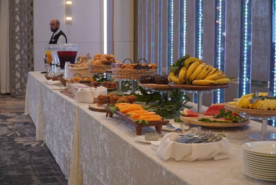 Buffet table with various fruits, pastries, and juice. A waiter stands nearby.