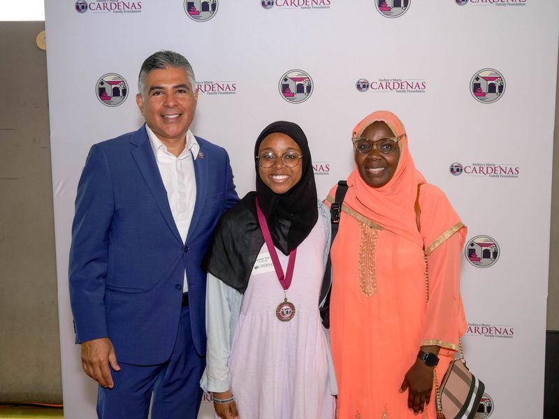 Three people pose in front of a backdrop with a logo.