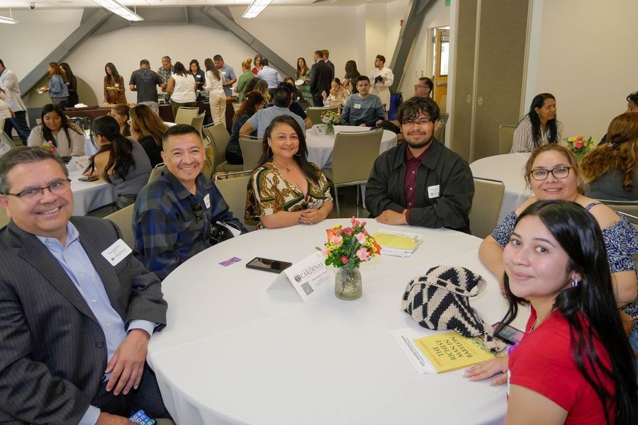 People seated at a round table, smiling at the camera, in a large room.