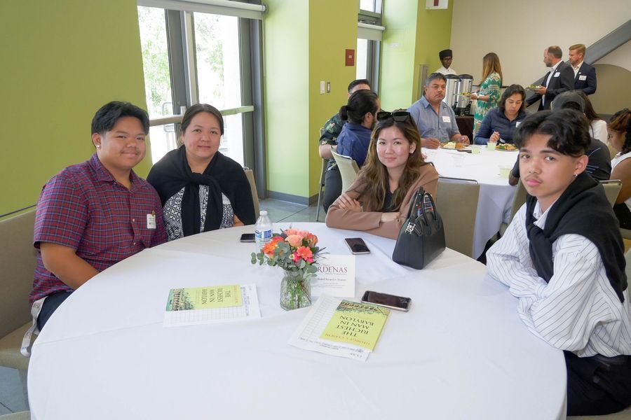 People seated at a round table, at an event with flowers and refreshments.