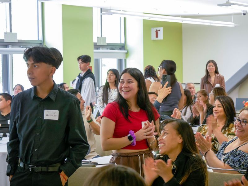 People clapping and smiling in a room. A young person in a black shirt looks toward the left.
