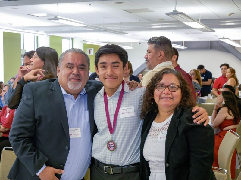 A young person wearing a medal poses with a smiling man and woman indoors.