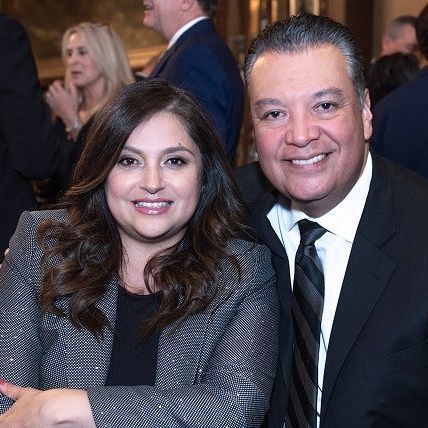 Woman and man smiling, both in professional attire. Woman in gray jacket, man in suit and tie.