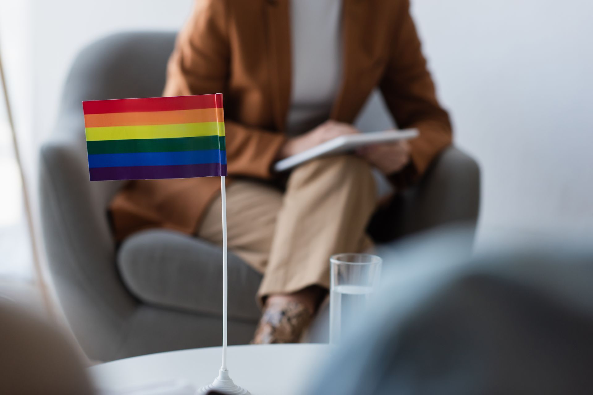 LGBTQ+ pride flag on a table; therapist in background.