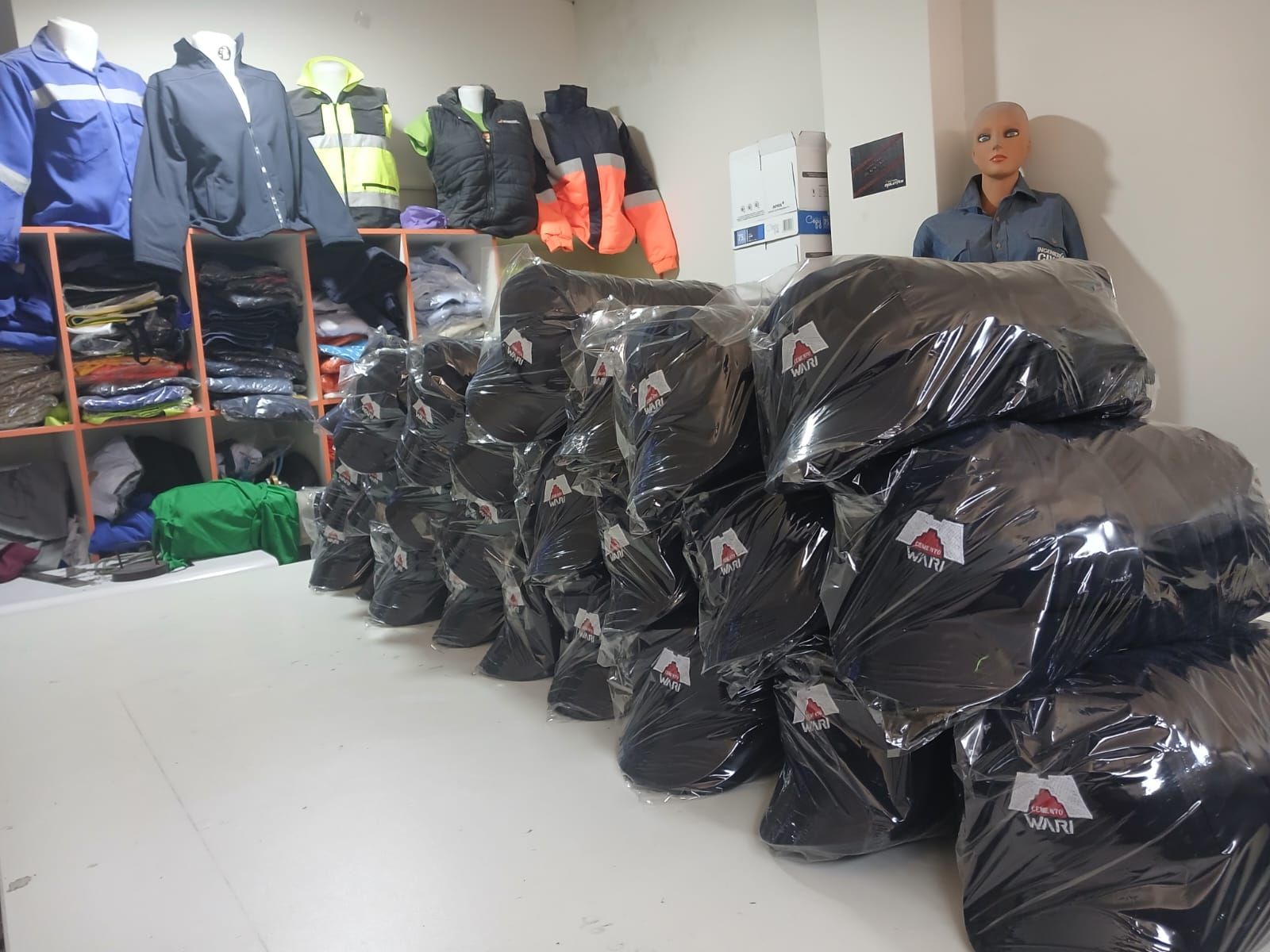 Montones de artículos en bolsas negras en un trastero, con estantes llenos de chaquetas y mochilas a la izquierda.