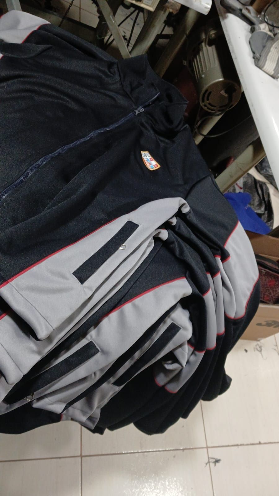 Pila de chaquetas negras y grises dobladas sobre un suelo de baldosas en un espacio interior desordenado.
