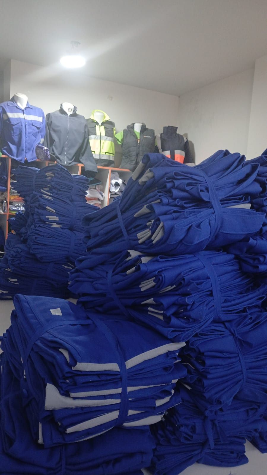 Montones de prendas azules dobladas en un almacén, con chaquetas colgadas en percheros al fondo.
