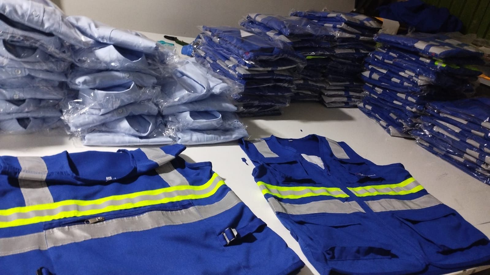 Montones de ropa de trabajo reflectante azul, extendida y apilada en un área de almacenamiento o almacén.