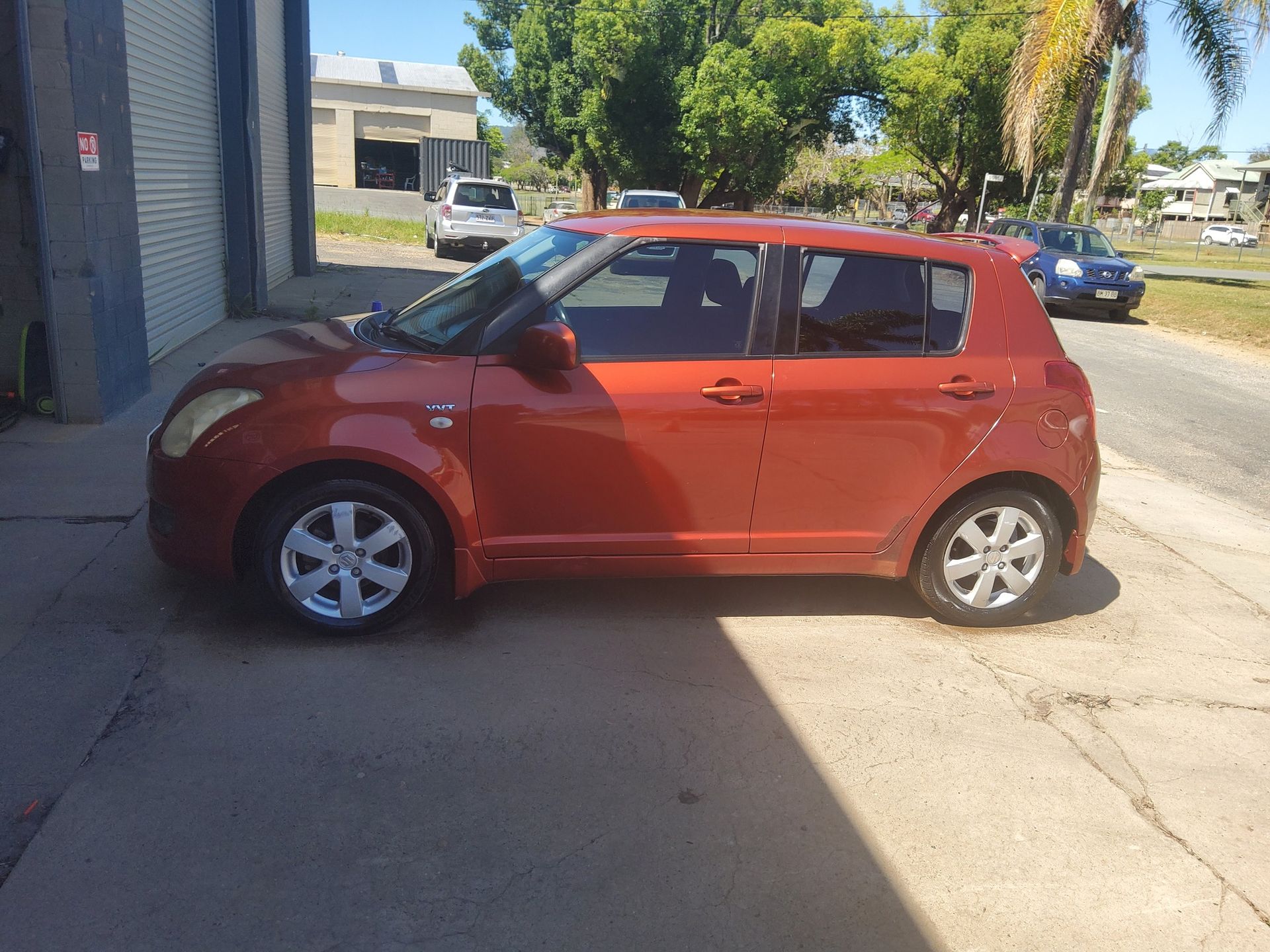 A red car is parked on the side of the road in front of a garage — Country Dirt Blasters Mobile Car Detailing In Murwillumbah, NSW