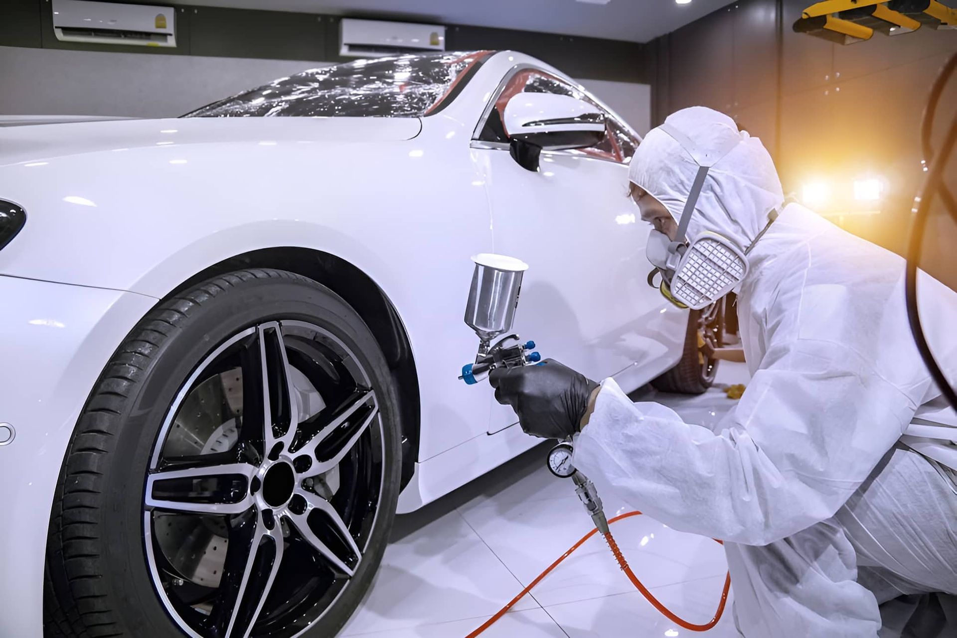 A Man In A Protective Suit Is Spray Painting A White Car — Country Dirt Blasters Mobile Car Detailing In Murwillumbah, NSW