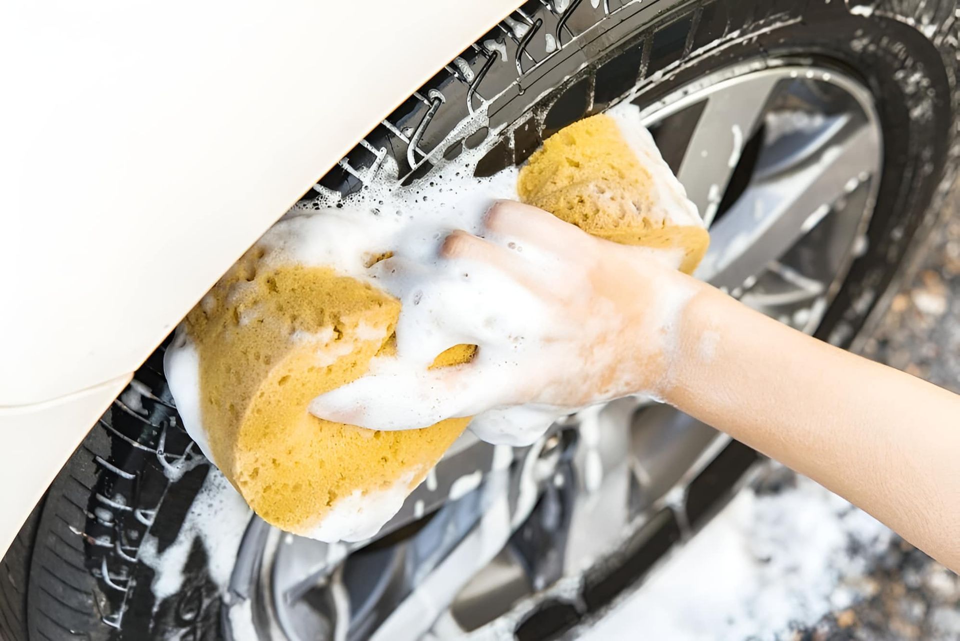 A Person Is Washing A Car Wheel With A Sponge — Country Dirt Blasters Mobile Car Detailing In Murwillumbah, NSW