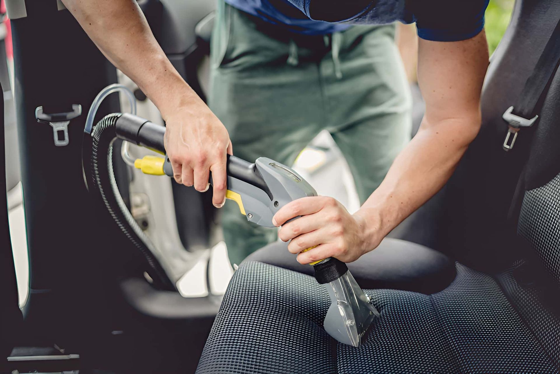 A Man Is Cleaning The Seats Of A Car With A Vacuum Cleaner — Country Dirt Blasters Mobile Car Detailing In Murwillumbah, NSW